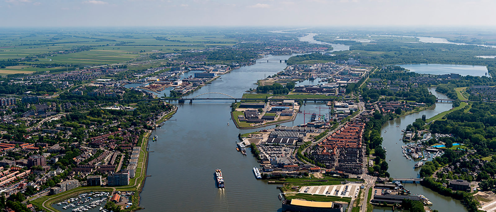 Een landschapsfoto van een rivier in Nederland. Op de foto zijn schepen op het water te zien, met langs de randen huizen.